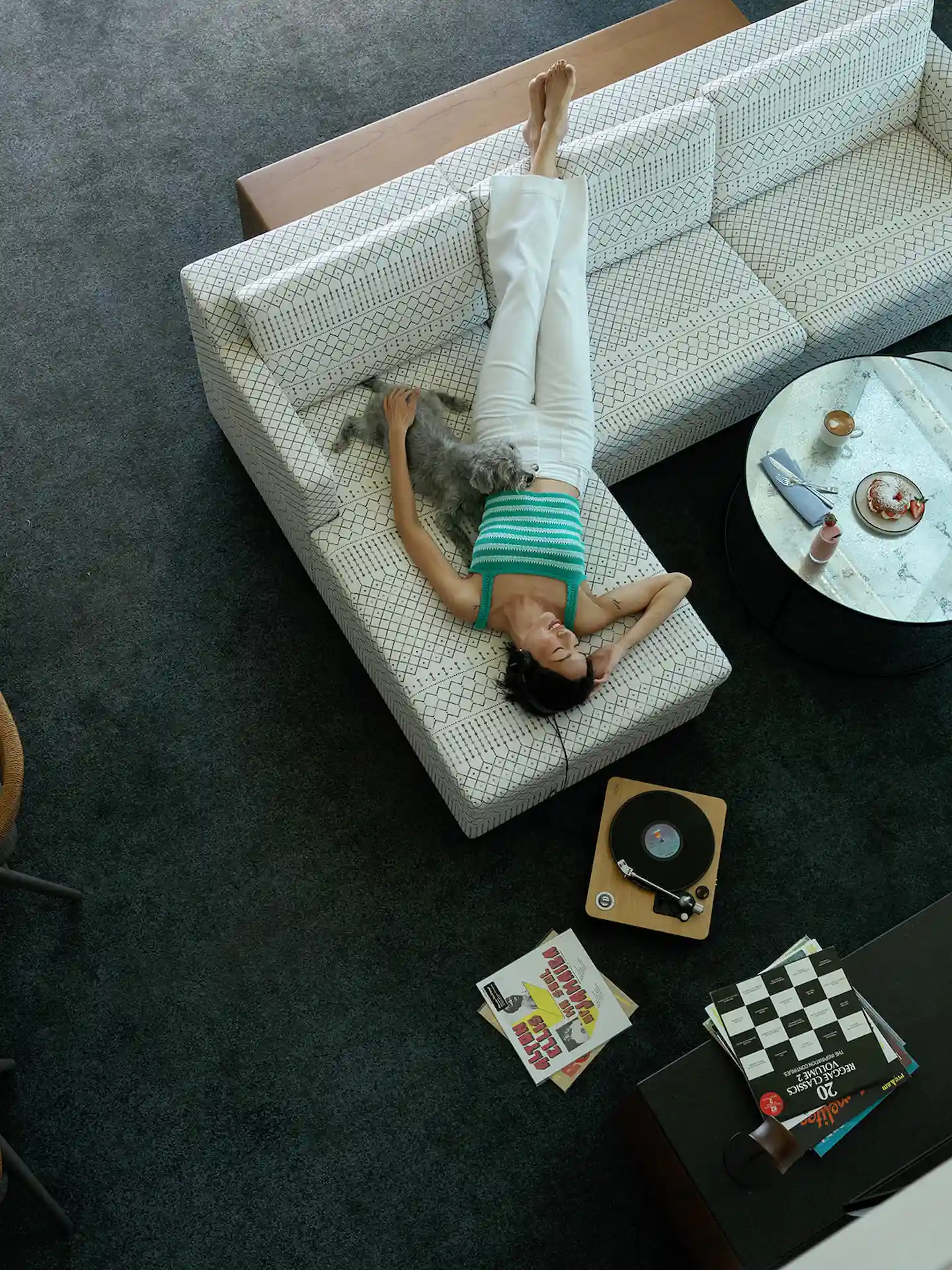 A woman lying on the sofa in the suite, listening to music with her dog by her side, enjoying a cozy and relaxing moment